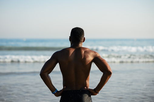 Back view of black fit sportsman towards the sea.  Strong man ready to get into the ocean for swimming.