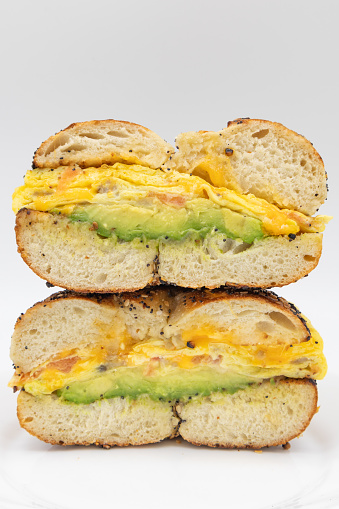 A New York City style bagel sandwich cut in half and stacked with eggs cheese and avocados