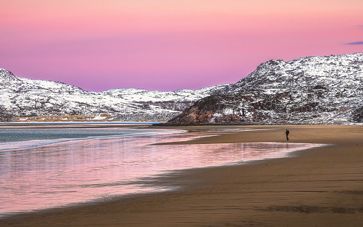 A silhouette, a figure on a beach. Amazing sunrise polar landscape with white snowy mountain range on the horizon. Arctic ocean panoramic view.