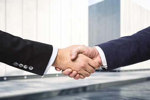 Handshake of two businessmen on the background of sunny exterior of the business center, signing of a contract concept, close up