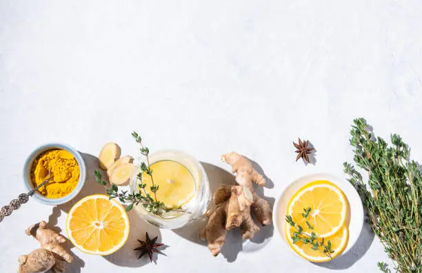 Photo of Immune boosting remedy. Flat lay  with ingredients from turmeric, thyme, lemon, star anise and glass water with lemon on white background with hard shadows.