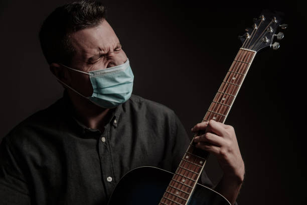 um homem com uma máscara médica em um fundo escuro, com um violão velho. - eastern european flash - fotografias e filmes do acervo