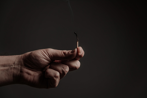 burning match in men's fingers, on a dark background. Close-up