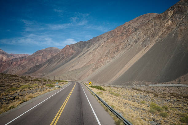 strada vuota con linea gialla nella valle, ande, provincia di mendoza, argentina - arid climate asphalt barren blue foto e immagini stock