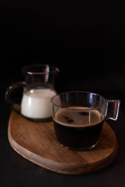Coffee cup and milk jug on a wooden table with black background.