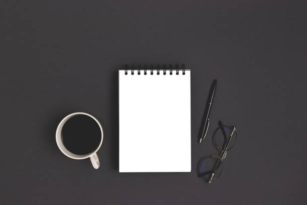 istock Workspace with open notepad mockup, stationery and coffee cup on a black background. 1297457546