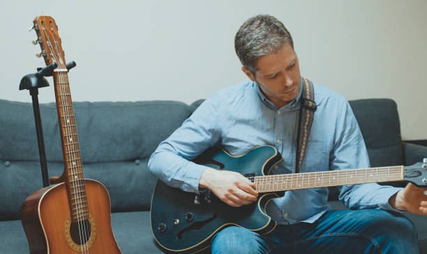 istock Handsome man tuning his semi-acoustic guitar indoors. 1297461823