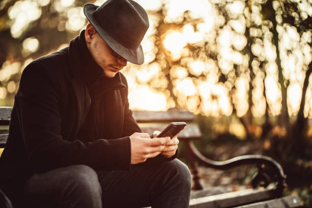 Handsome man with hat checking messages on phone in park