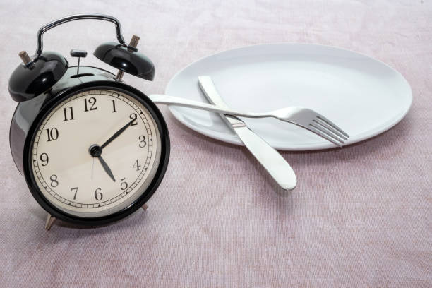 Weight loss or dieting concept of an alarm clock on a dinner plate Weight loss or dieting concept of an alarm clock on a dinner plate fasting stock pictures, royalty-free photos & images