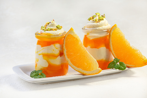 Dessert of low-fat cottage cheese and orange mousse is served in glass jars with pieces of pistachio and fresh mint. Concept of healthy nutrition.