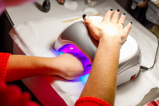 Woman's hand in a lamp for manicure. Dries nails after polishing. UV LED lamp.