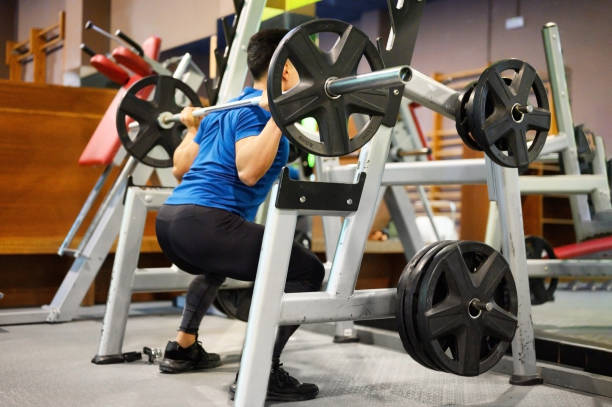 si adatta all'uomo che fa squat in una macchina da allenamento. foto di alta qualità - crouching barbell weightlifting weight training foto e immagini stock