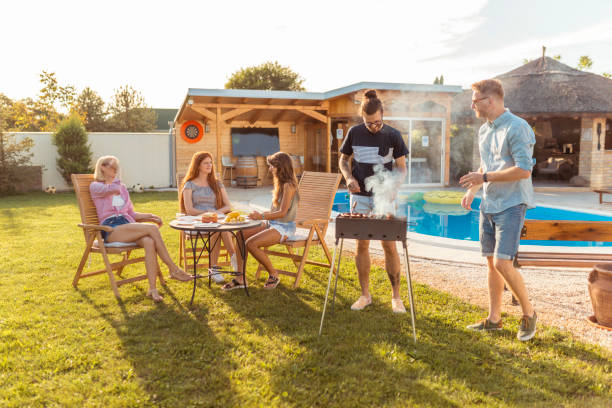 Friends grilling meat and having fun at backyard poolside barbecue party Group of young friends having a backyard barbecue party, grilling meat and having fun while spending sunny summer day outdoor by the swimming pool garden parties stock pictures, royalty-free photos & images