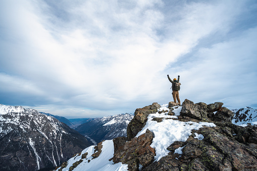 Men standing on top of the snowy mountain, his hands are raised