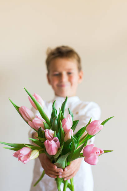 istock Young boy, kid child hands with pink tulips, flowers 1297479780