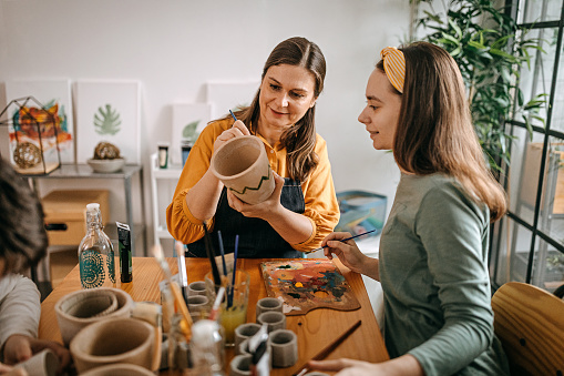 Mature woman is painting pottery with her daughter in her art studio
