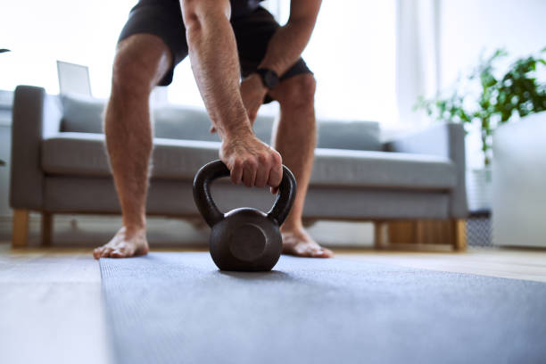 primo piano dell'uomo che afferra kettlebell durante gli esercizi di allenamento a casa - barefoot foto e immagini stock