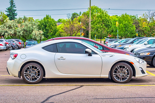 A white colored Scion FR-S sports car is parked in a parking lot in Hamilton, Ontario, Canada on an overcast day. Due to the discontinuation of the Scion marque, in August 2016 the FR-S was re-branded as the Toyota 86 for the 2017 model year and onward