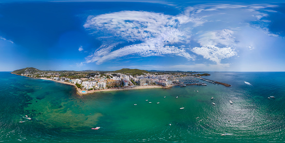 Aerial drone 360 Degree panoramic sphere aerial photo of the beautiful beach front of Ibiza in Spain showing the Spanish beach and harbour with boats in the ocean from above