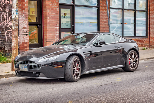 A black colored Aston Martin V8 Vantage luxury sports car is parked on a street in Toronto, Ontario, Canada on an overcast day.