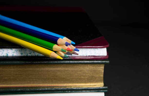 istock Colored pencils, ledger, and books with black background 1297486518