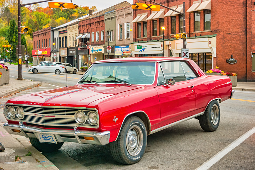 A red colored 1965 Chevrolet Chevelle Malibu SS muscle car is parked on the main street in Paris, Ontario, Canada in the evening.