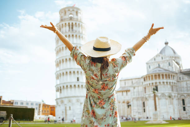 Seen from behind tourist woman in floral dress rejoicing Seen from behind tourist woman in floral dress with hat near Leaning Tower in Pisa, Italy with open arms rejoicing. pisa stock pictures, royalty-free photos & images