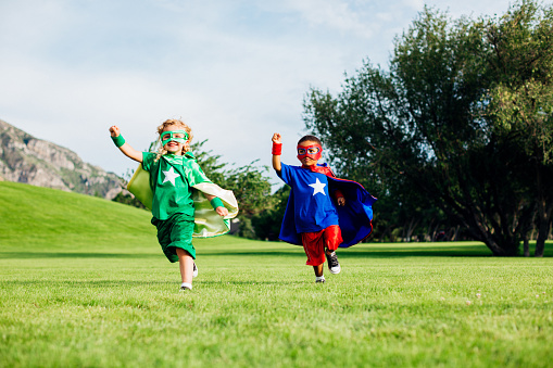 A boy and girl, dressed as superheroes in capes and masks, imagine conquering foes and fears while running to freedom.
