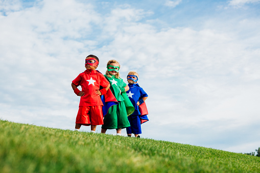 A team of superheroes comprised of children work as a team to show their neighborhood strength and confidence. They are dressing up and using their imagination by wearing capes and masks.