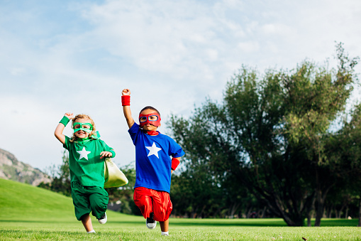 A boy and girl, dressed as superheroes in capes and masks, imagine conquering foes and fears while running to freedom.