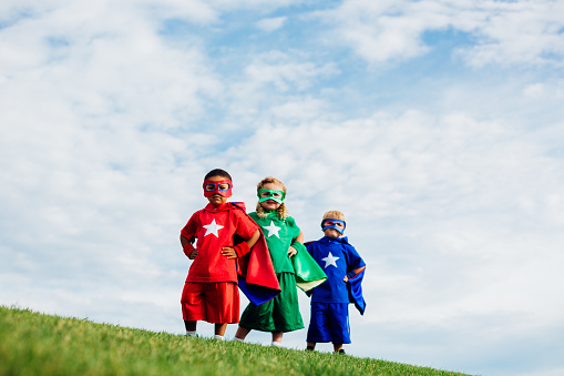 A team of superheroes comprised of children work as a team to show their neighborhood strength and confidence. They are dressing up and using their imagination by wearing capes and masks.