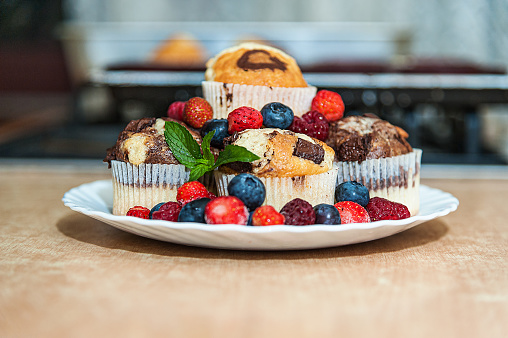 Close-up Photo of Tasty Muffins Made of Chocolate Placed on a Plastic Dish with Different Berry Fruit Served on a Wooden Table in the Kitchen.