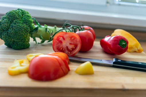 Kitchen Knife, Cutting Board and Tomatoes, Peepers, and Broccoli on the Wooden Cutting Board in the Kitchen. Close-up Photo of Preparation of Food with no People.