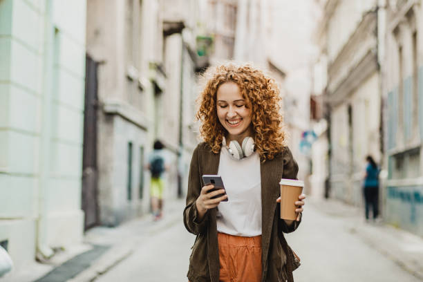 Young woman is using mobile phone on the move and holing reusable coffee cup