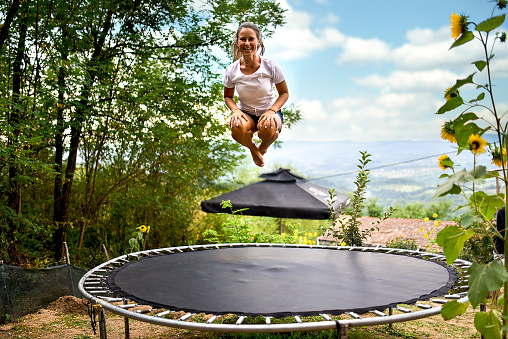 Smiling young woman in the backyard of her house jumps on a trampoline