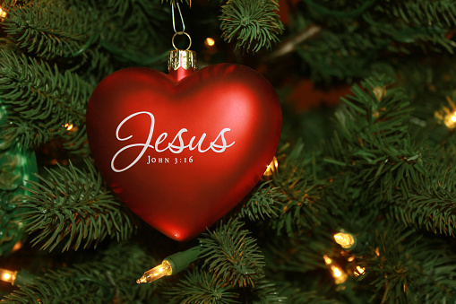 Red heart shaped Jesus Christmas ornament on tree with light