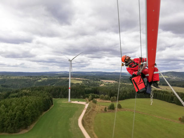 istock Epic view on Industrial climber,  rope access technician working on tip of the wind turbine blade, checking serrations and trailing edge and looking up, windfarm and country side behind him 1297501529