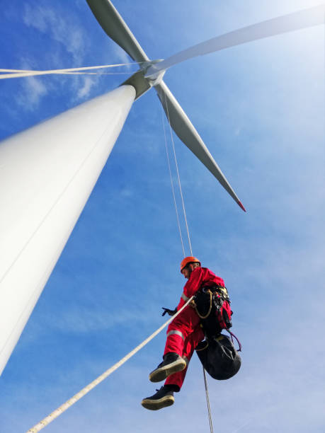 istock View from bottom on wind-turbine and rope access technicians abseiling with equipment down from blade on the ropes, dramatic sky and sunny day. 1297501532