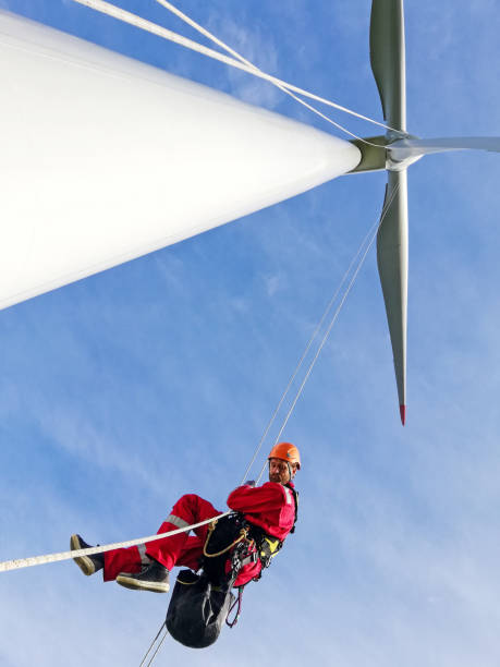View from bottom wind-turbine and industrial climber rope access technicians abseiling down from blade on the ropes, looking down, dramatic sky and sunny day. stock photo
