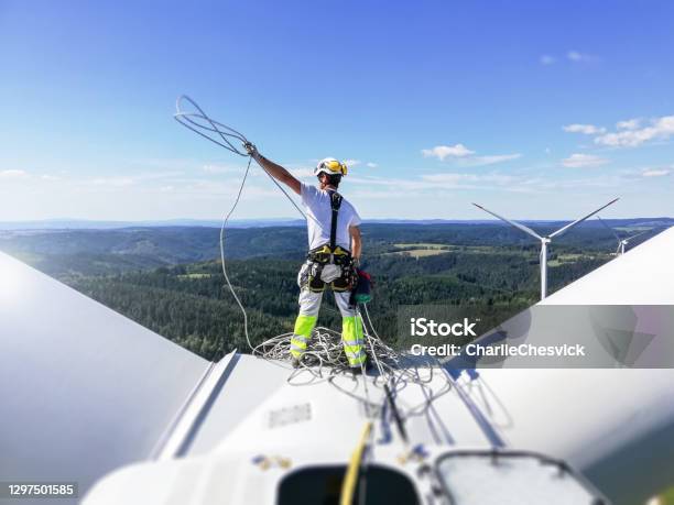 Rear View On Professional Rope Access Technician Standing On Roof Of Wind Turbine And Pulling Rope Up Sun Is Behind Wind Turbine Stock Photo - Download Image Now