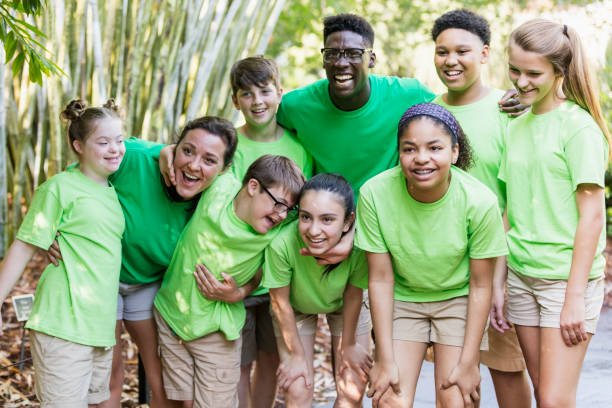 Summer camp including two down syndrome children Multi-ethnic children having fun at summer camp on a field trip to a park. A camp counselor, a mid adult woman in her 30s, is standing between an 11 year old girl and 12 year old boy who both have down syndrome. summer camp photos stock pictures, royalty-free photos & images