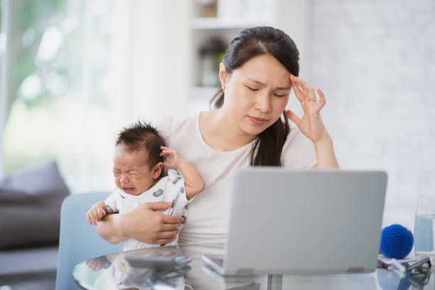 Oh, this baby would not stop crying! A new mother who is also working from home appears stressed as she is holding her baby who is also crying. She is resting her head on her hand while looking at the laptop screen in front of her. money cry stock pictures, royalty-free photos & images
