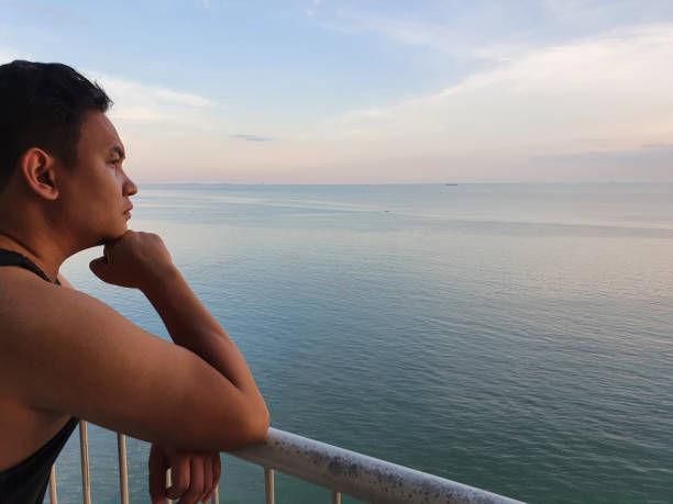 istock Asian man looking to the ocean from balcony at dawn or sunset, thinking gesture 1297517178