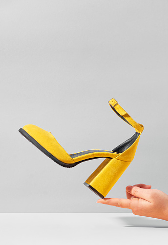 Yellow high-heeled suede shoe balancing on the finger of female hand.