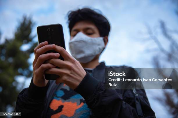 A Young Man With Mask Using His Mobile Phone Outdoors Stock Photo - Download Image Now