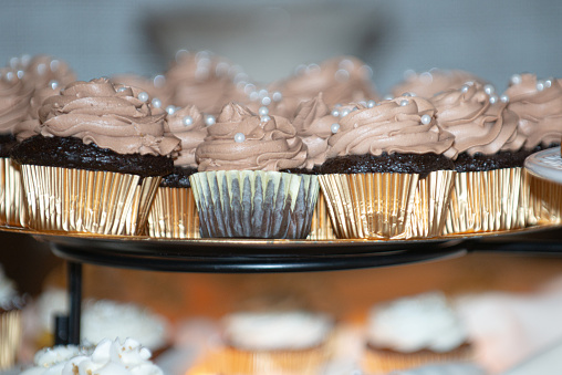 Chocolate cupcakes with chocolate frosting and pearl srinkles in gold paper cups