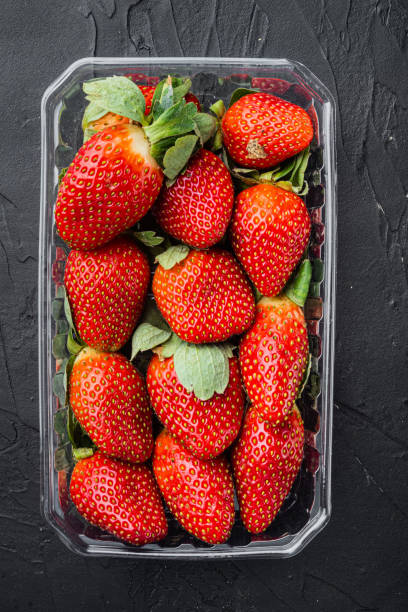 istock Transparent plastic tray with freshly picked strawberries, on black background, top view flat lay 1297532067