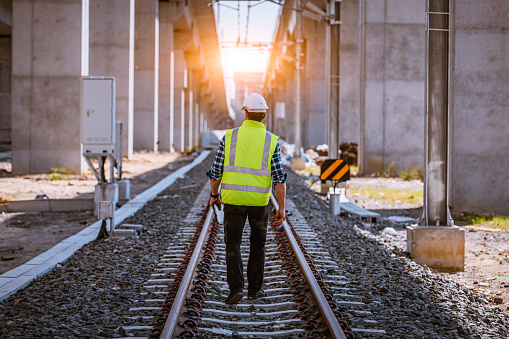 Engineer railway under inspection and checking construction process train and railroad station .Engineer wearing safety uniform and helmet by holding document in work.