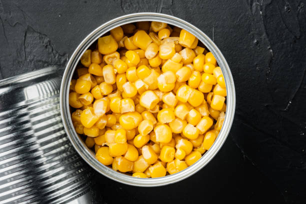 istock Sweet corn grains in tin can, on black background, top view flat lay 1297532809