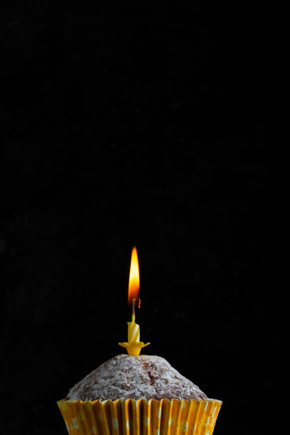 istock upcake in a paper cup with a yellow candle with flame on a dark background copy space birthday greeting card 1297532862